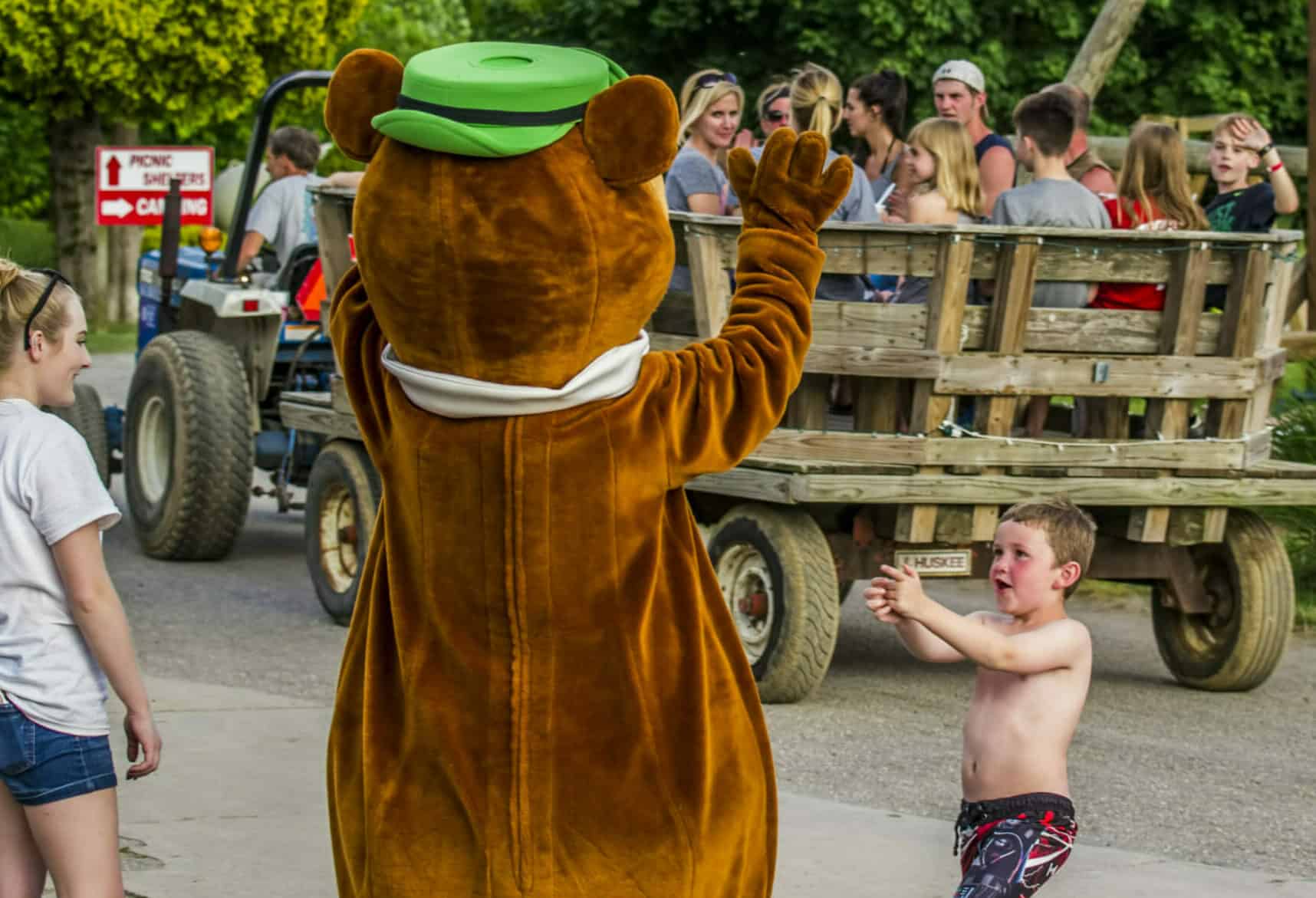 A teddy bear mascot is waving to a young boy in front of a crowd.
